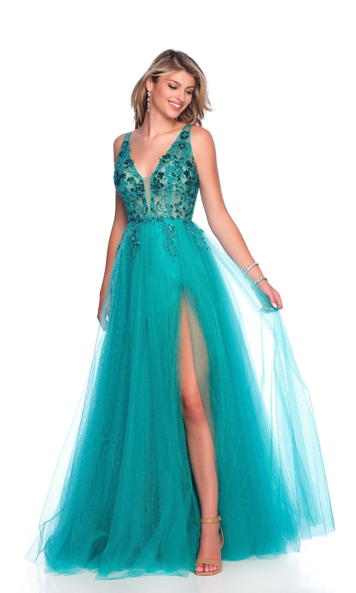A woman models the Dave and Johnny 12027 long prom dress—sleeveless and teal blue, with an embroidered sheer bodice, deep V neckline, high slit, and flowing A-line tulle skirt—while standing and holding the skirt.